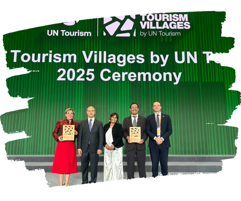 Cinco representantes posan con las placas del premio Best Tourism Villages 2025 frente al fondo verde de la ceremonia de UN Tourism